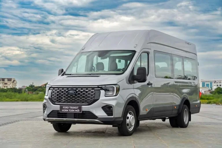 Xe Ford Transit 16 chỗ màu trắng đang chạy trên đường, minh họa sự phổ biến và khả năng vận hành của mẫu xe.