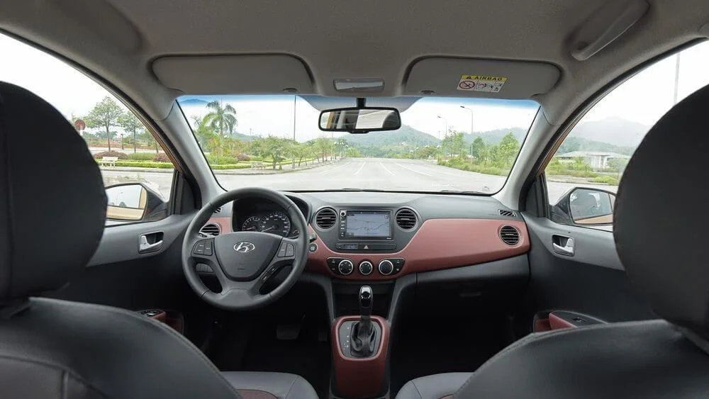 Hình ảnh nội thất Hyundai i10 với các nút điều khiển, vô lăng và bảng đồng hồ hiển thị các tính năng an toàn.