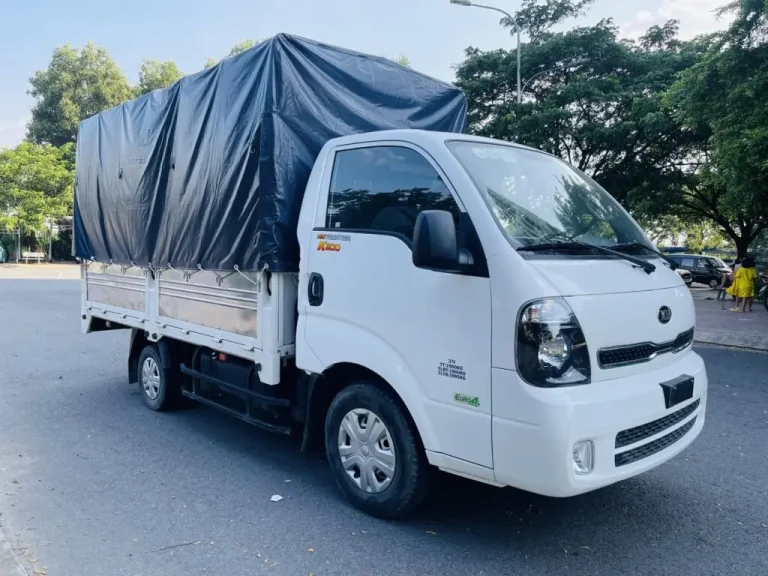 Hình ảnh xe tải Kia K200 cũ màu trắng với thùng mui bạt đang chạy trên đường, minh họa tính đa dụng của xe.