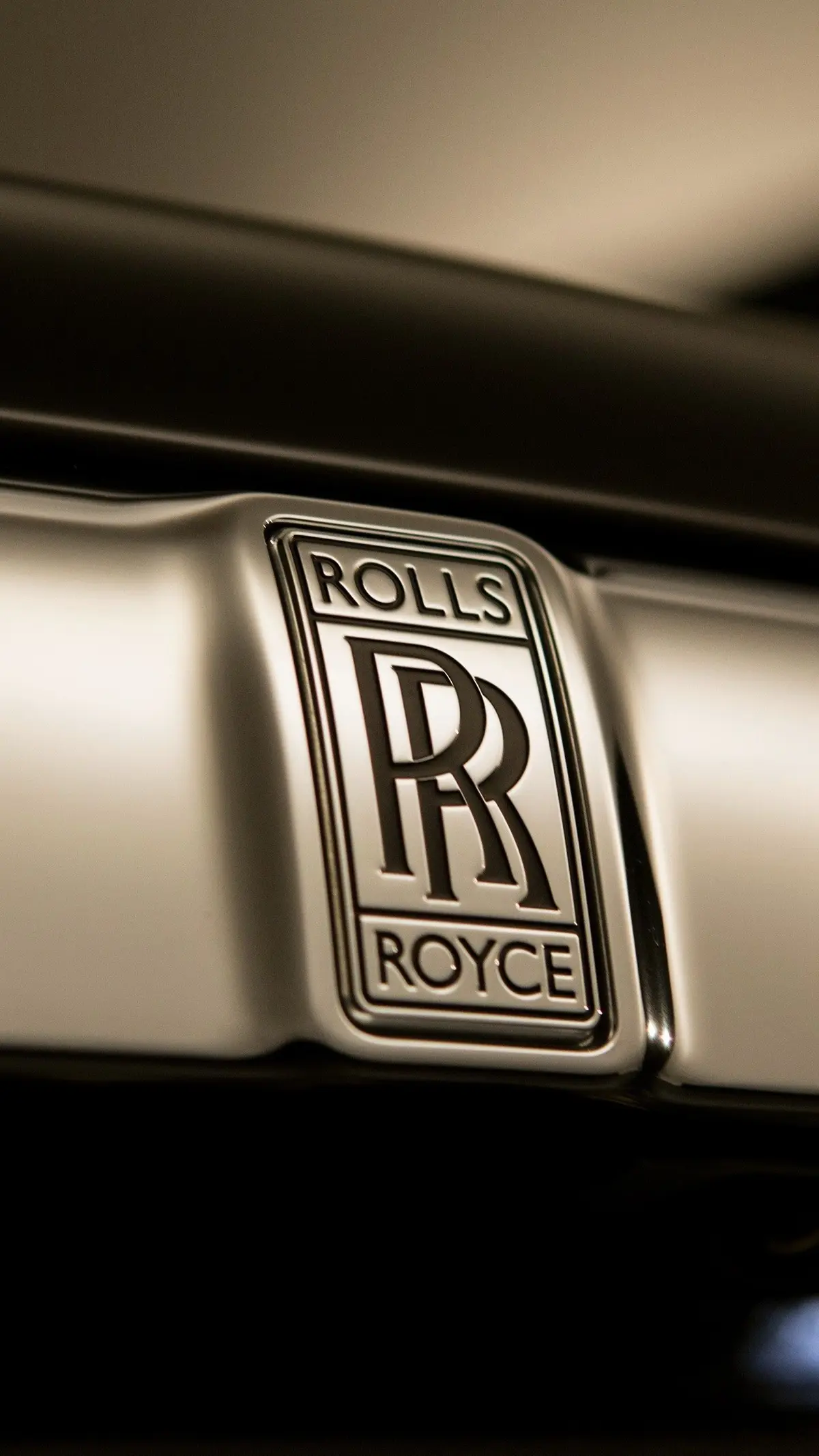 Hình ảnh cận cảnh logo Rolls-Royce, với hai chữ R lồng vào nhau, trên nền lưới tản nhiệt chrome sáng bóng của một chiếc xe.