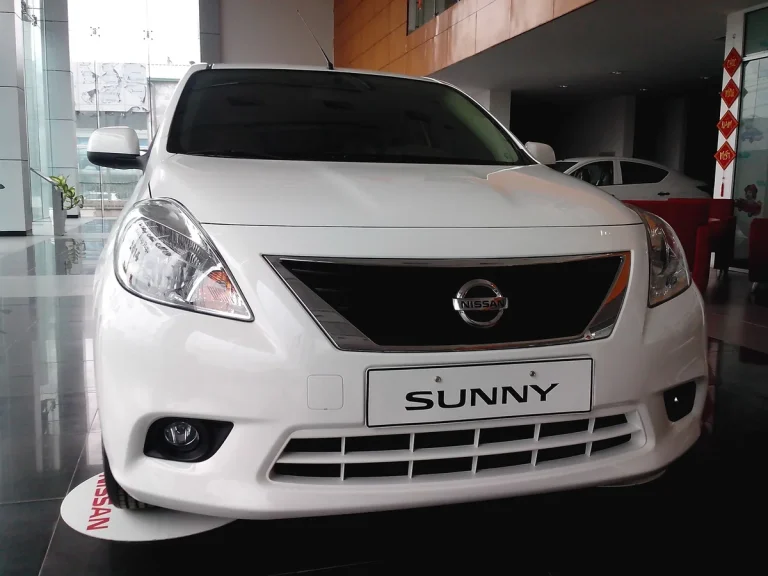 Hình ảnh xe Nissan Sunny cũ màu trắng đang di chuyển trên đường phố Việt Nam, cho thấy thiết kế tổng thể của xe.