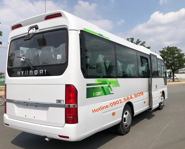 Hình ảnh xe khách Hyundai County 29 chỗ Tracomeco 2026 màu trắng, đang di chuyển trên đường phố Việt Nam.